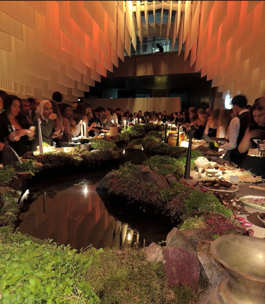 Immersive dining event table styled with water, moss, and warm lighting