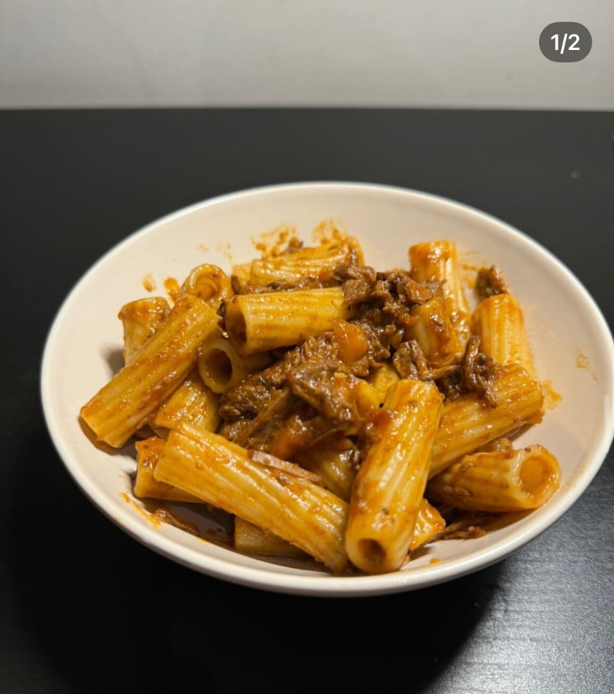 Beef ragu rigatoni in a white bowl on a dark table