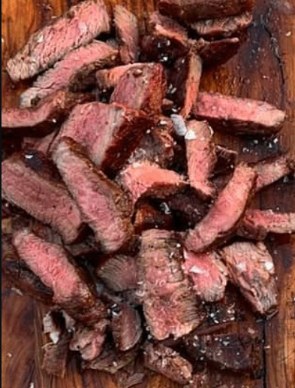 Sliced ribeye glistening on a dark wood board