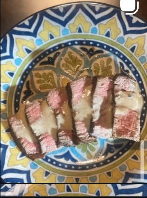 Sliced steak with cream sauce on a patterned plate